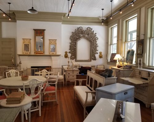 A bright, vintage-style room with wooden floors, elegant furniture, and decorative mirrors.