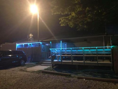 A dimly lit building at night with blue neon lights, featuring a wooden deck and a parked car nearby.