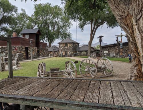 A rustic outdoor scene featuring wooden wagons, stone buildings, and lush greenery under a clear sky.
