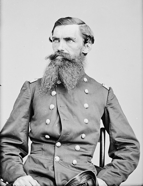 A seated man in a military uniform with a prominent beard, looking confidently at the camera.