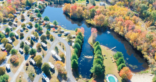 Aerial view of a colorful autumn landscape with a pond, surrounded by RVs and trees in vibrant fall foliage.