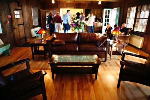 A cozy wooden interior with a leather sofa, coffee table, and people socializing in the background.
