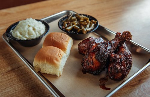 A metal tray with two pieces of fried chicken, mashed potatoes, green beans, and two dinner rolls.
