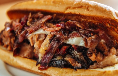 A close-up of a hearty sandwich filled with layers of smoked meat and toppings, served in a soft bun.