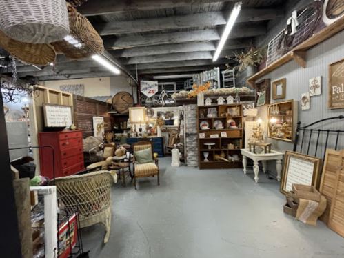 A cozy vintage shop filled with various antiques, furniture, and decor items under soft lighting.