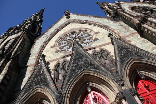 Gothic-style church facade with intricate stonework, pointed arches, and a large rose window against a clear blue sky.