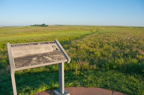 A grassy landscape with a historical sign about a significant event, under a clear blue sky.