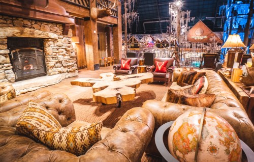 Cozy lodge interior with a stone fireplace, wooden furniture, and a globe, featuring rustic decor and warm lighting.