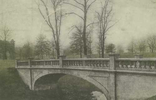 A vintage photo of a stone bridge with decorative railings, surrounded by trees in a serene landscape.