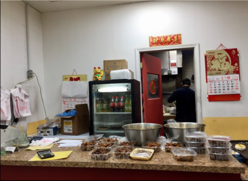A busy kitchen counter with food containers, a fridge, and a chef working in the background. Chinese decorations on the wall.