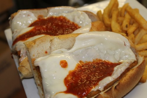 Two toasted sandwiches topped with melted cheese and marinara sauce, served with a side of golden French fries.