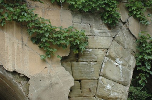 Close-up of a weathered stone archway with cracks, partially covered by green ivy.