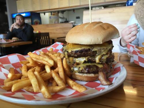 A towering cheeseburger with three patties and bacon, served with a side of golden fries on a plate.