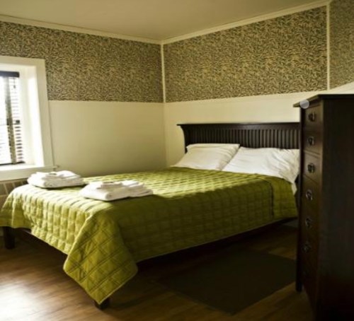 Cozy bedroom featuring a green quilted bedspread, two towels, and patterned wallpaper.