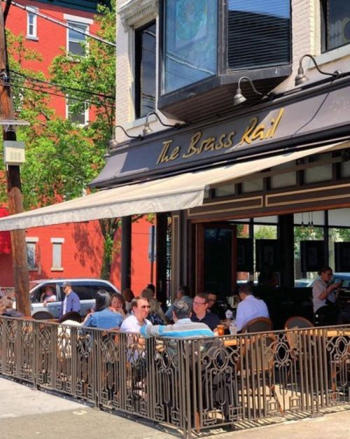 Outdoor dining scene at The Brass Rail, with patrons enjoying meals on a sunny day.