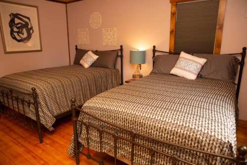 A cozy bedroom with two metal-framed beds, gray bedding, and a lamp on a nightstand. Decor includes wall art.