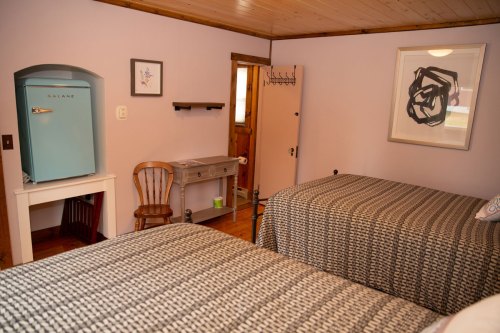 A cozy bedroom with two beds, wooden walls, and a mirror reflecting a door, creating a warm, inviting atmosphere.