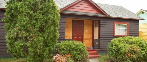 A cozy house with a red door, surrounded by green shrubs and trees, featuring a mix of dark and light wood siding.