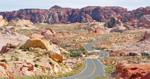 Winding road through colorful desert landscape with rocky formations and distant mountains under a clear sky.