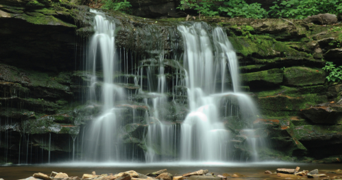 A serene waterfall cascading over moss-covered rocks, surrounded by lush greenery.