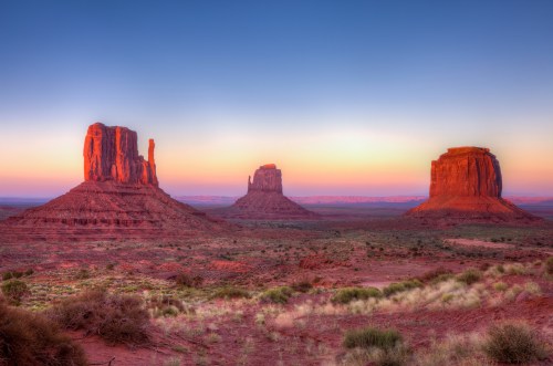 A scenic view of Monument Valley at sunrise, featuring iconic red rock formations against a colorful sky.