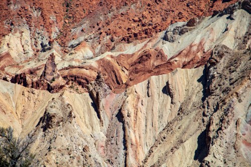 Colorful layered rock formations with shades of red, orange, and cream, showcasing geological textures and patterns.