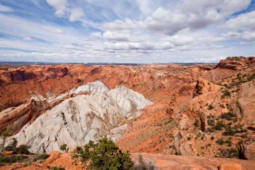 A panoramic view of colorful rock formations and clouds in a vast desert landscape.