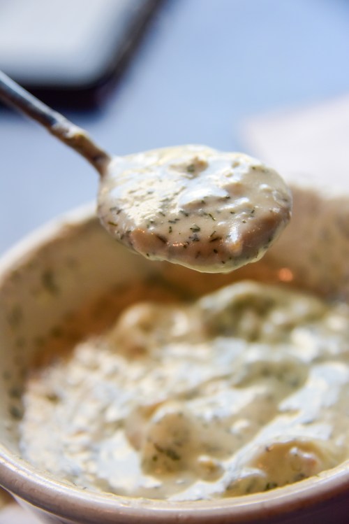 A spoonful of creamy sauce with herbs, hovering above a bowl filled with the same sauce.