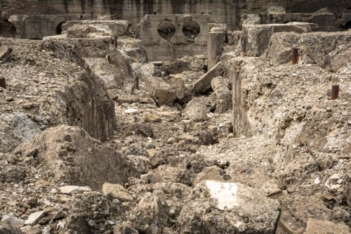 A desolate landscape of rubble and debris, with large concrete structures partially visible among the stones.