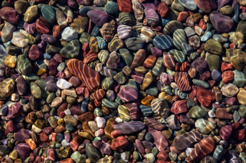 A colorful array of smooth, polished stones submerged in clear water, reflecting light and creating vibrant patterns.