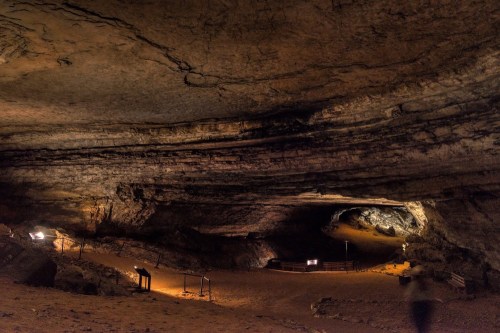 A dimly lit cave interior with rocky walls, pathways, and informational signs along the ground.