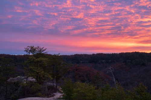 A vibrant sunset paints the sky in shades of pink and purple over a forested landscape.