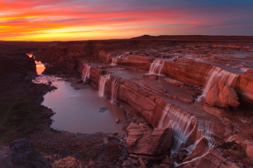 A stunning sunset over a canyon with cascading waterfalls and a river, reflecting vibrant colors in the sky.