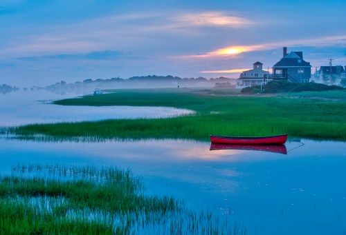 A serene landscape featuring a red canoe on calm water, surrounded by lush green grass and a misty sunset sky.