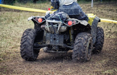 A person riding a muddy yellow ATV on a dirt track, with dirt flying from the rear tires.