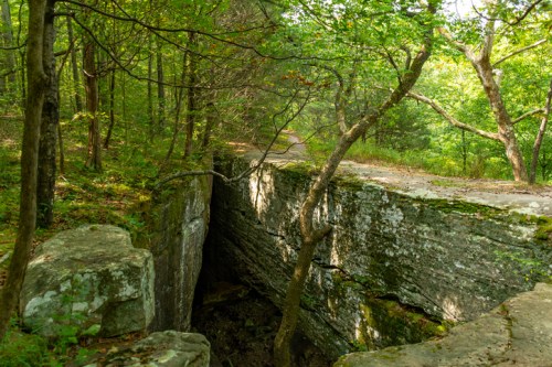 A rocky crevice surrounded by lush green trees and a path in a serene forest setting.