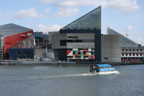 A water taxi glides across the water near modern buildings with geometric designs and colorful facades.