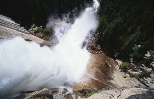 Aerial view of a powerful waterfall cascading over rocky cliffs into a lush forest below.