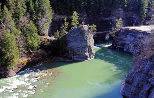 A serene river flows through a rocky canyon, surrounded by lush green trees and steep cliffs.