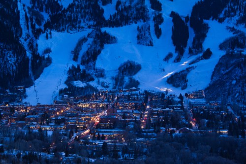A snowy mountain town illuminated at night, with ski slopes and twinkling lights in the valley below.