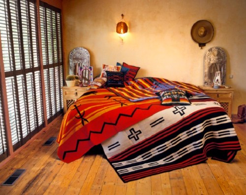 Cozy bedroom featuring a colorful patterned blanket on a wooden bed, with warm lighting and rustic decor.