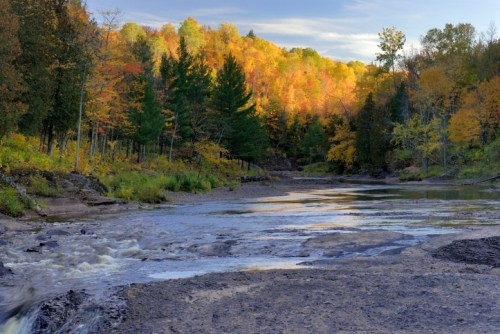A serene river flows through a colorful autumn landscape with vibrant trees and a clear sky.