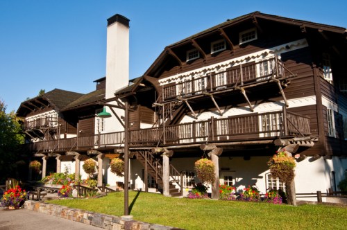 A charming wooden building with balconies, surrounded by colorful flower pots and a clear blue sky.
