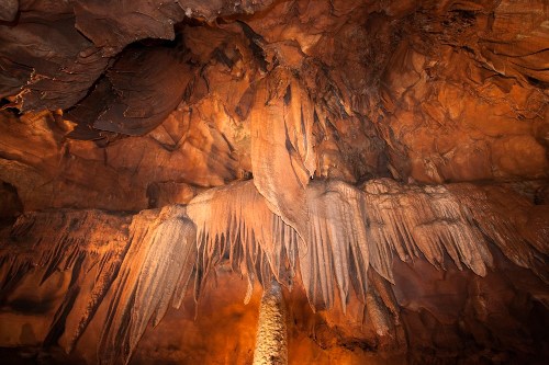 Stalactites and stalagmites in a dimly lit cave, showcasing intricate rock formations and textures.