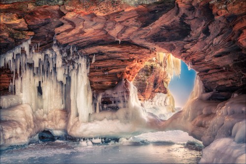 A frozen cave with icicles hanging from the rocky ceiling, leading to a bright light in the distance.