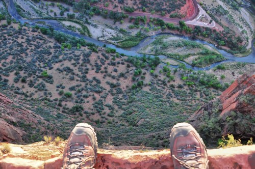 A pair of hiking boots at the edge of a cliff, overlooking a winding river and lush green landscape below.