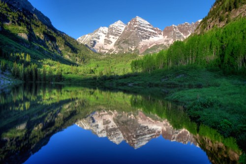 A serene mountain landscape with snow-capped peaks reflecting in a calm lake, surrounded by lush greenery.