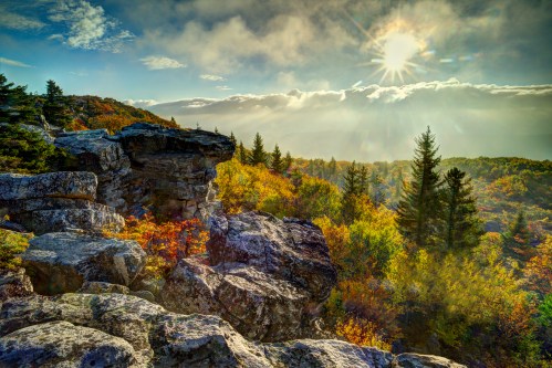 A scenic landscape featuring rocky outcrops, vibrant autumn foliage, and a bright sun shining through clouds.
