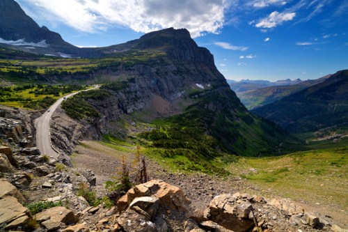 A scenic view of a winding road along a mountainous landscape with lush greenery and dramatic cliffs under a blue sky.