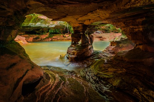 A serene cave with smooth rock formations and a tranquil water pool reflecting warm colors.